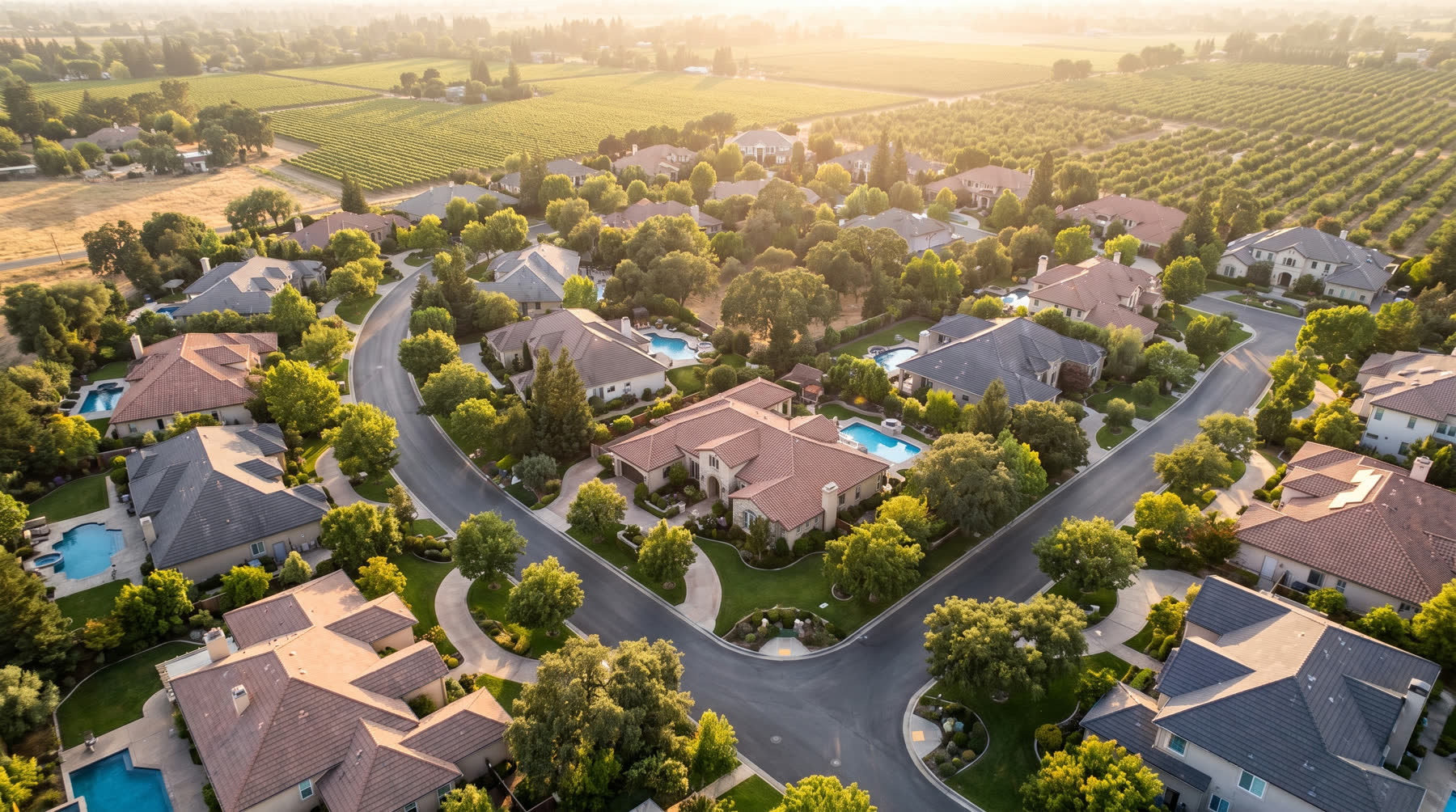 Aerial view of an upscale Yuba-Sutter neighborhood backing onto orchards at golden hour